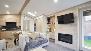 A modern living room with a fireplace, a dining area, and a kitchen with wooden cabinetry. - Host Stay Hideaway Retreat (York)