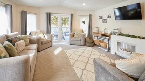 Ein Wohnzimmer mit einer Sofagarnitur, einem Kamin, einem Fernseher und Blick ins Freie durch eine Glastür.