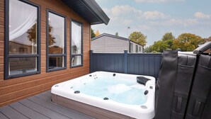 Ein Whirlpool auf einer Holzterrasse mit Blick auf ein Haus und Bäume.