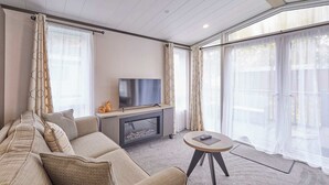 A modern living room with a sofa, a flat-screen TV, a fireplace, and large windows with sheer curtains. - Host Stay Royal Pines Lodge (York)