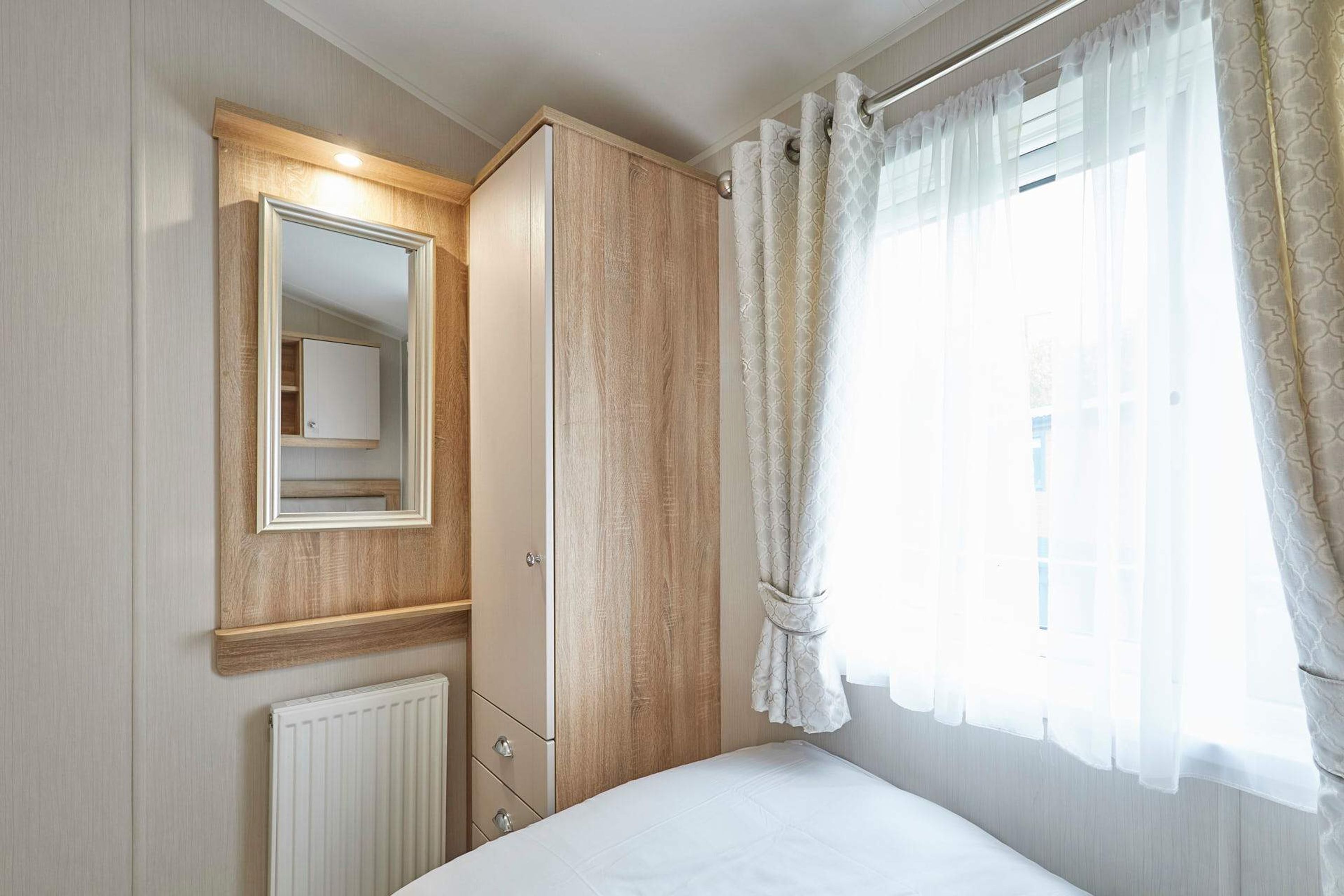A bedroom with a bed, a wardrobe, a mirror, a radiator, and a window with curtains.