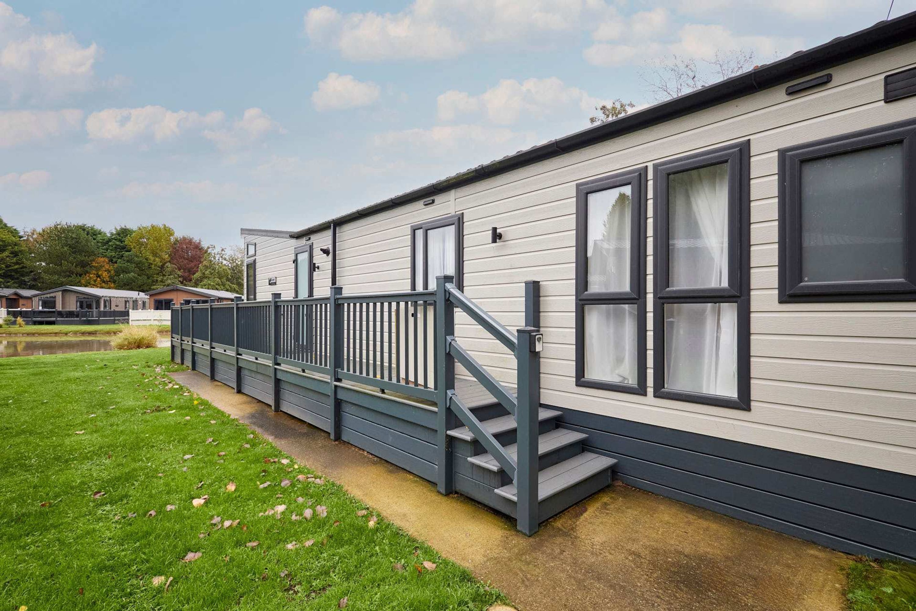 A mobile home with a grey exterior, a grey staircase leading to a balcony, and a small pond in the background.