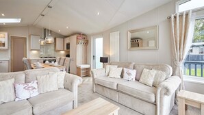 Un salón espacioso con un conjunto de sofá color beige, una mesa de centro de madera y un amplio ventanal con cortinas.
