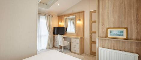 A hotel bedroom with a bed, a desk with a chair, a television, a mirror, and a framed picture on the wall.