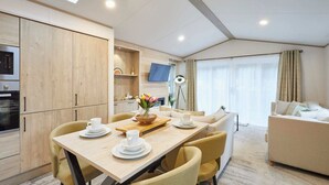 A modern kitchen with wooden cabinets, a dining table with chairs, and a sofa in a living area with a large window. - Host Stay Wag Tail Lodge (York)