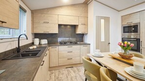 A modern kitchen with wooden cabinets, a gas stove, and a dining area with a table set for two. - Host Stay Wag Tail Lodge (York)