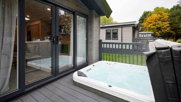A hot tub on a wooden deck with a sliding glass door leading to a living area. - Host Stay Wag Tail Lodge (York)