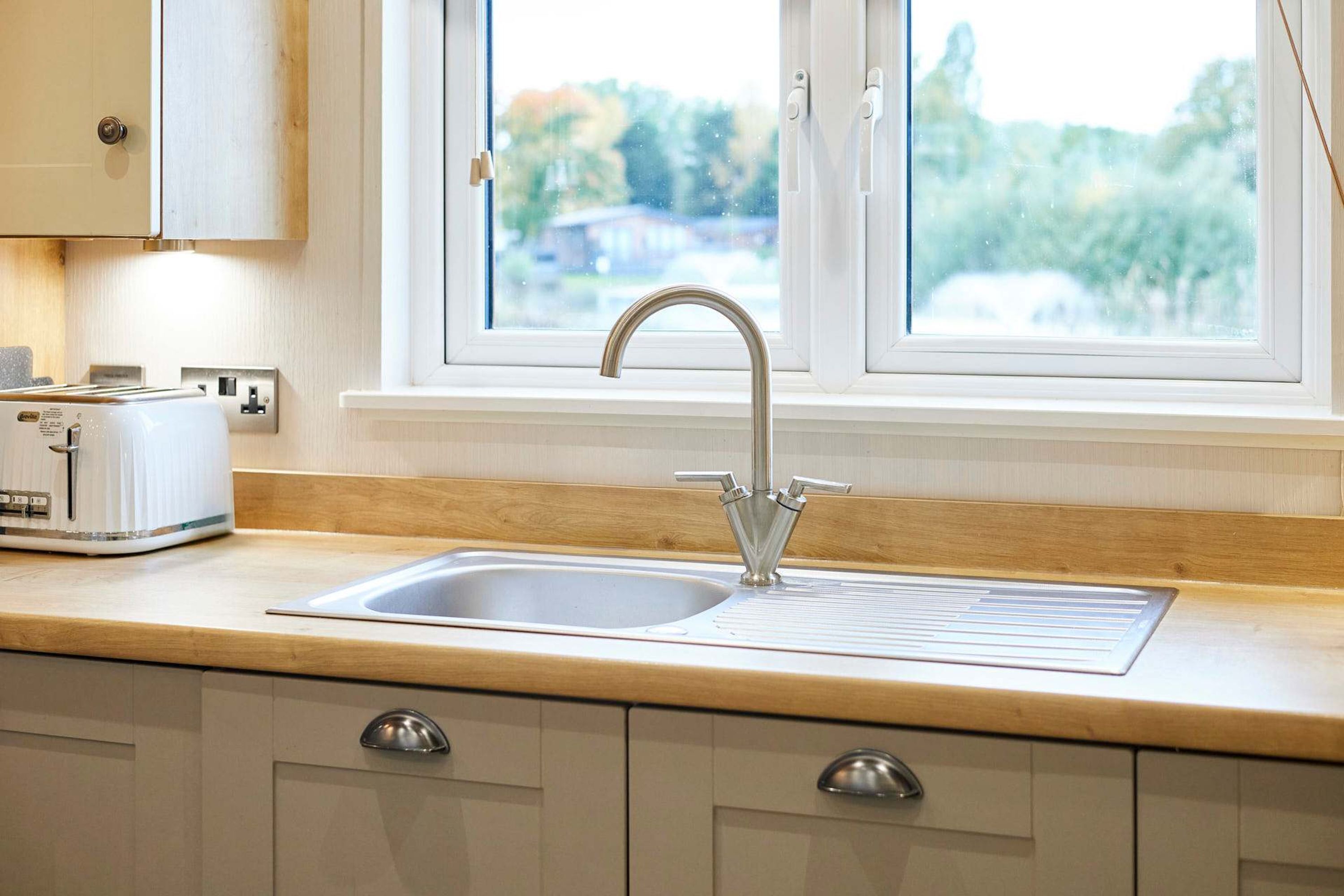 A kitchen with a stainless steel sink, a window with a view of trees, and a toaster on the countertop.