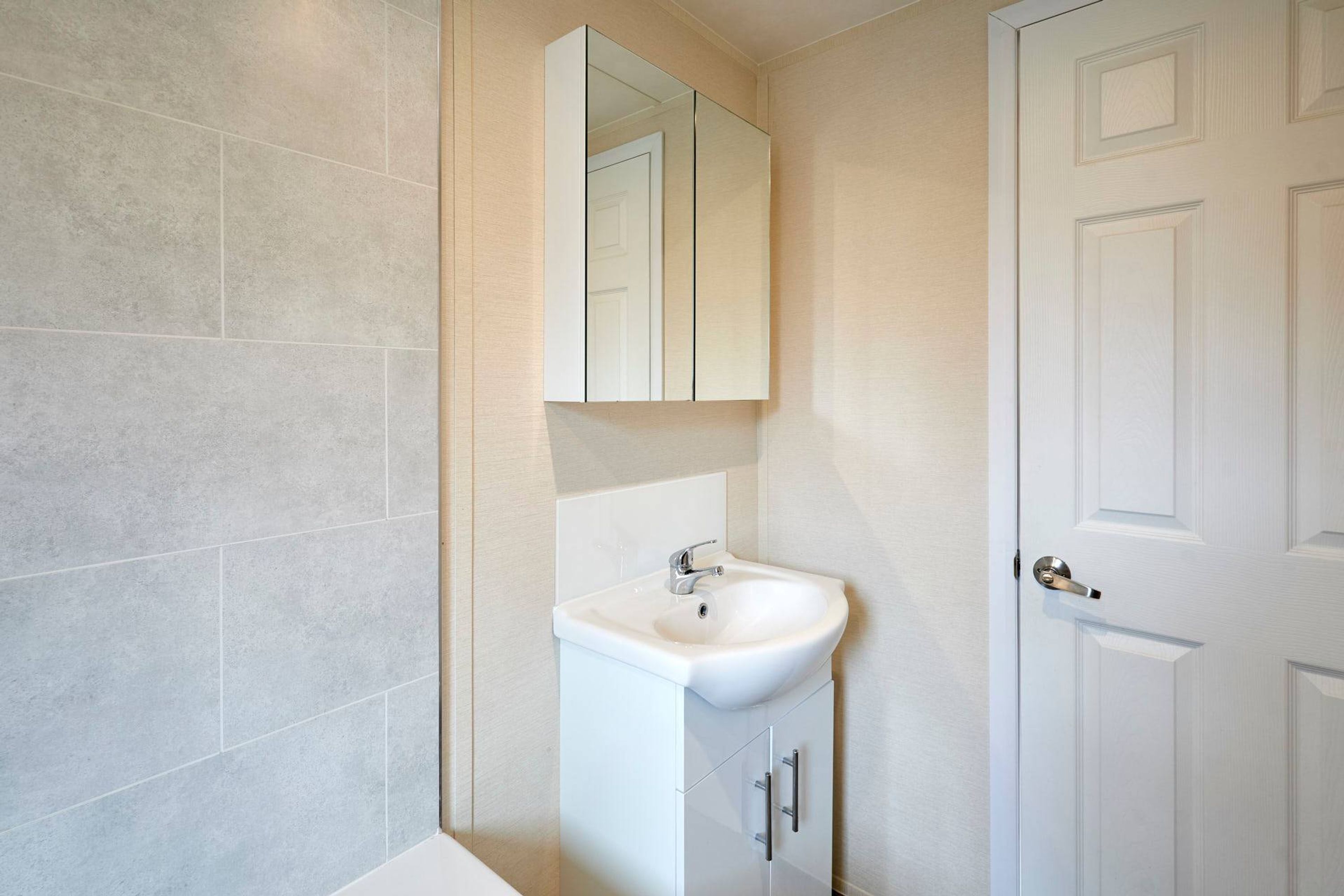 A bathroom with a white sink, a mirror above it, and a door to the right.