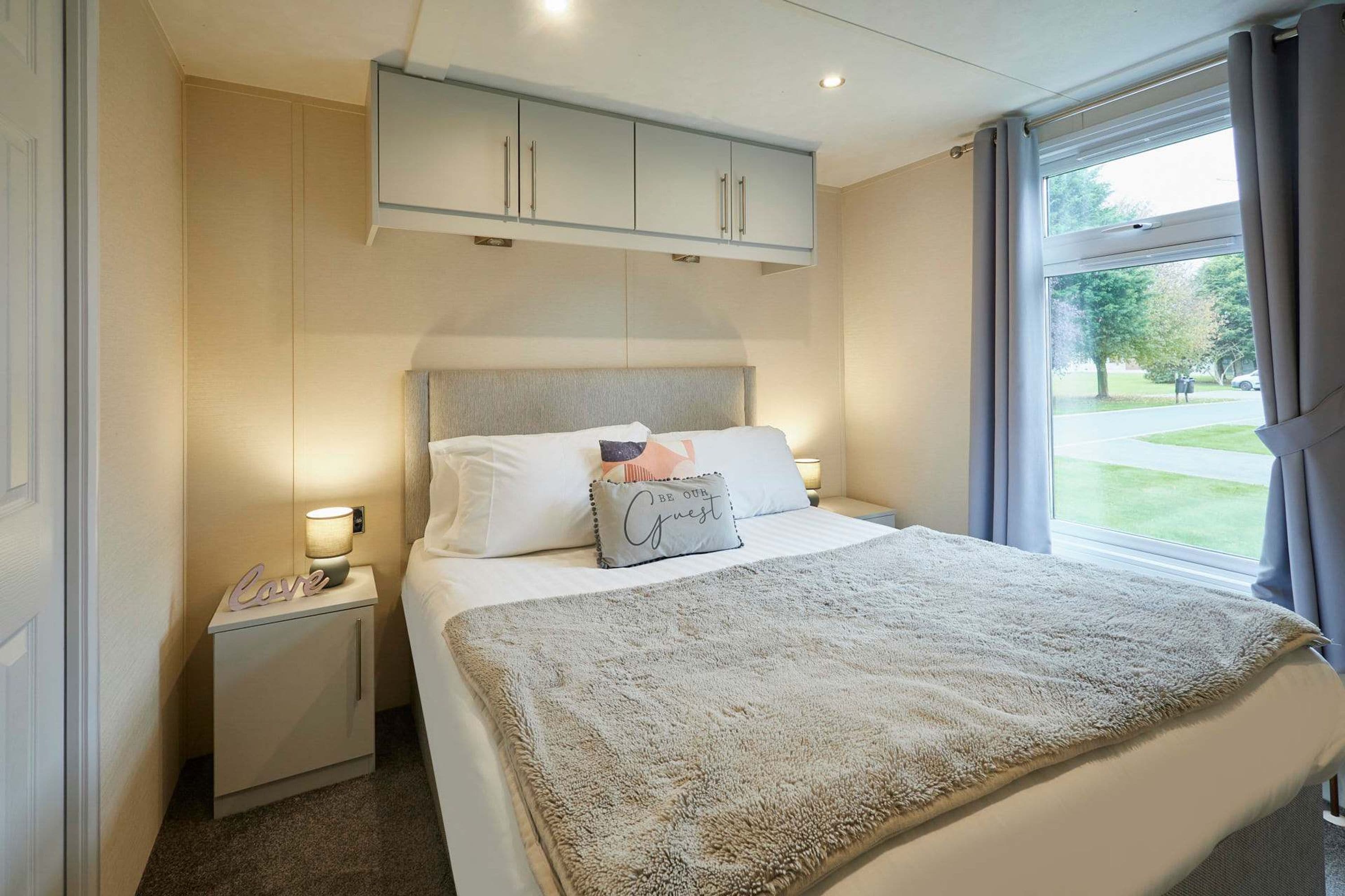 Un dormitorio ordenado con cama, lámparas de noche, mesitas de noche, un armario y una ventana con cortinas.