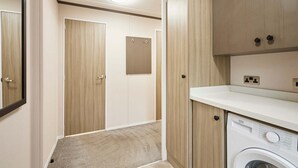 A laundry room with a front-loading washing machine, wooden cabinets, and a mirror. - Host Stay Gleneagles Lodge (York)