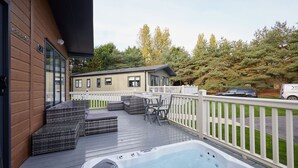 A deck with a hot tub, wicker furniture, and a view of a building and trees. - Host Stay Gleneagles Lodge (York)