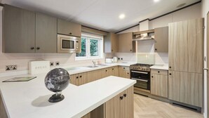 A modern kitchen with wooden cabinets, a built-in microwave, a gas stove, and a large island with a globe decoration. - Host Stay Gleneagles Lodge (York)