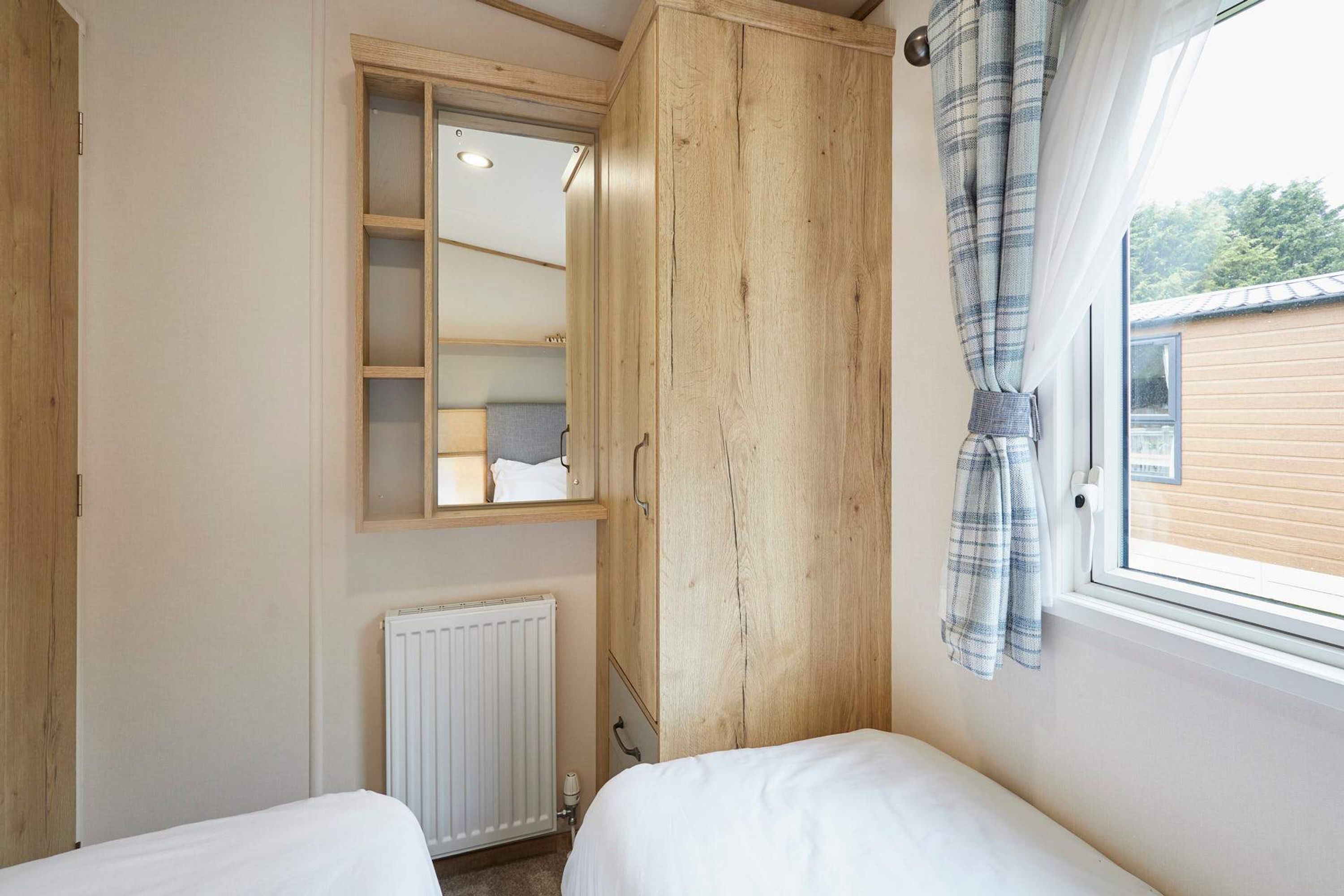 Ein Schlafzimmer mit Holzschrank, Spiegel, Heizkörper und einem blickdichten Fenster.