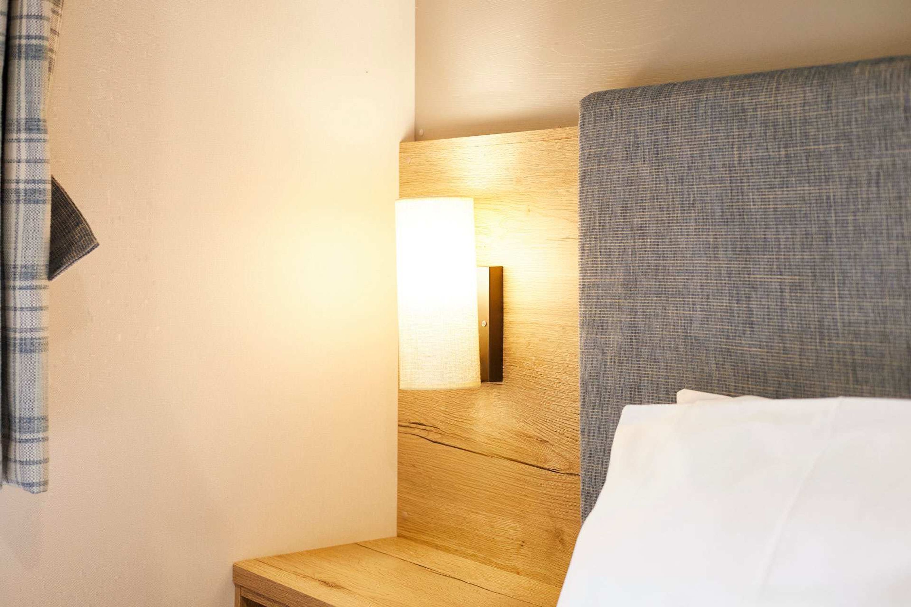 Una camera d'albergo con un poggiatesta in legno, una lampada da comodino e una tenda a quadri.