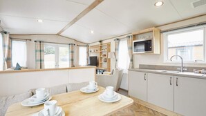 A cozy, well-lit room with a wooden dining table set for tea, a kitchenette with a microwave, and a window with curtains. - Host Stay Squirrel Lodge (York)