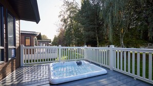 Una vasca idromassaggio su un pontile di legno, con un recinto bianco e alberi sullo sfondo.