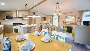 Un'accogliente cucina ben illuminata con elettrodomestici moderni, una zona pranzo con tavolo in legno apparecchiata per quattro persone e un angolo salotto confortevole con divano e poltrone.