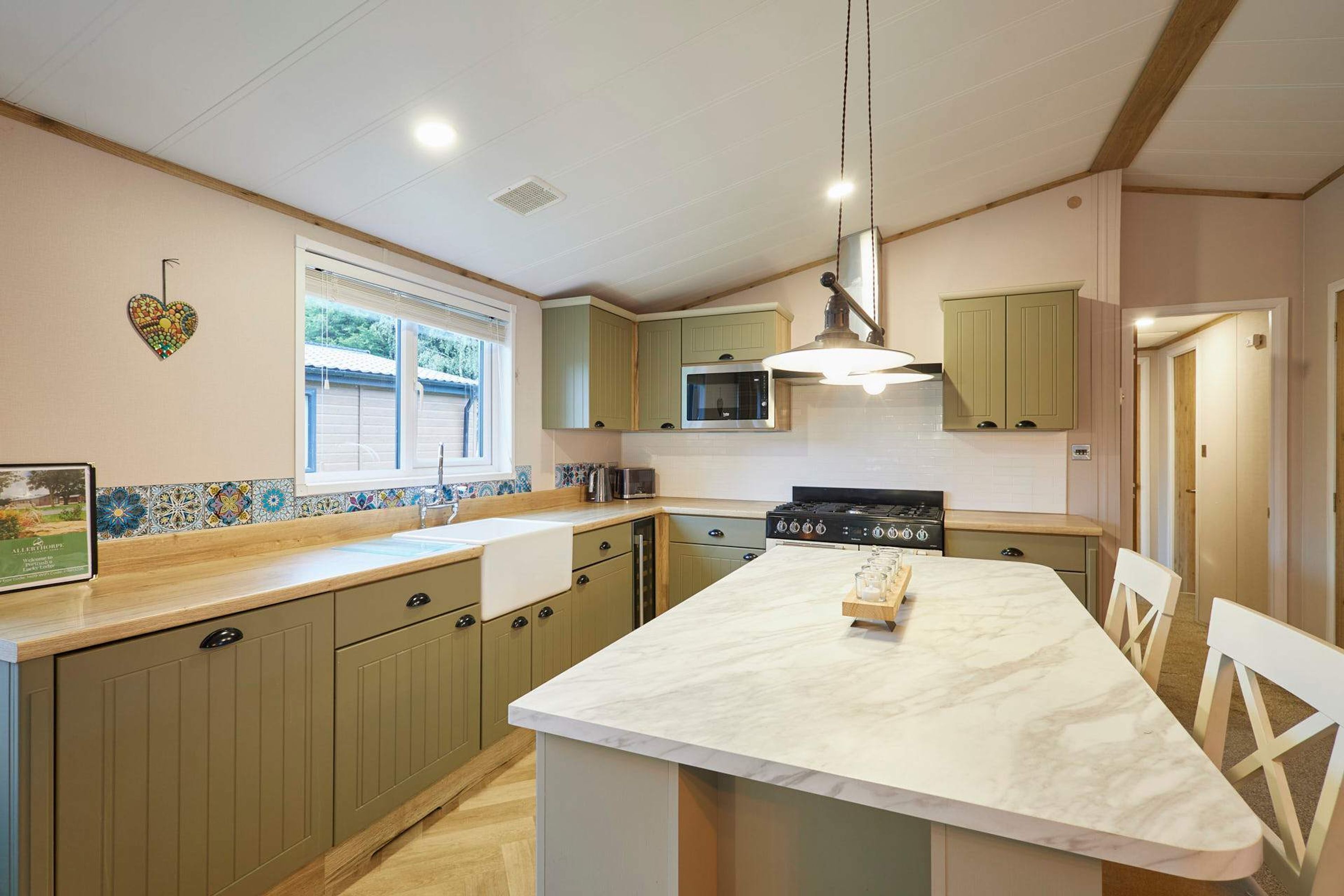 A kitchen with a marble island, green cabinets, a microwave, and a stove.