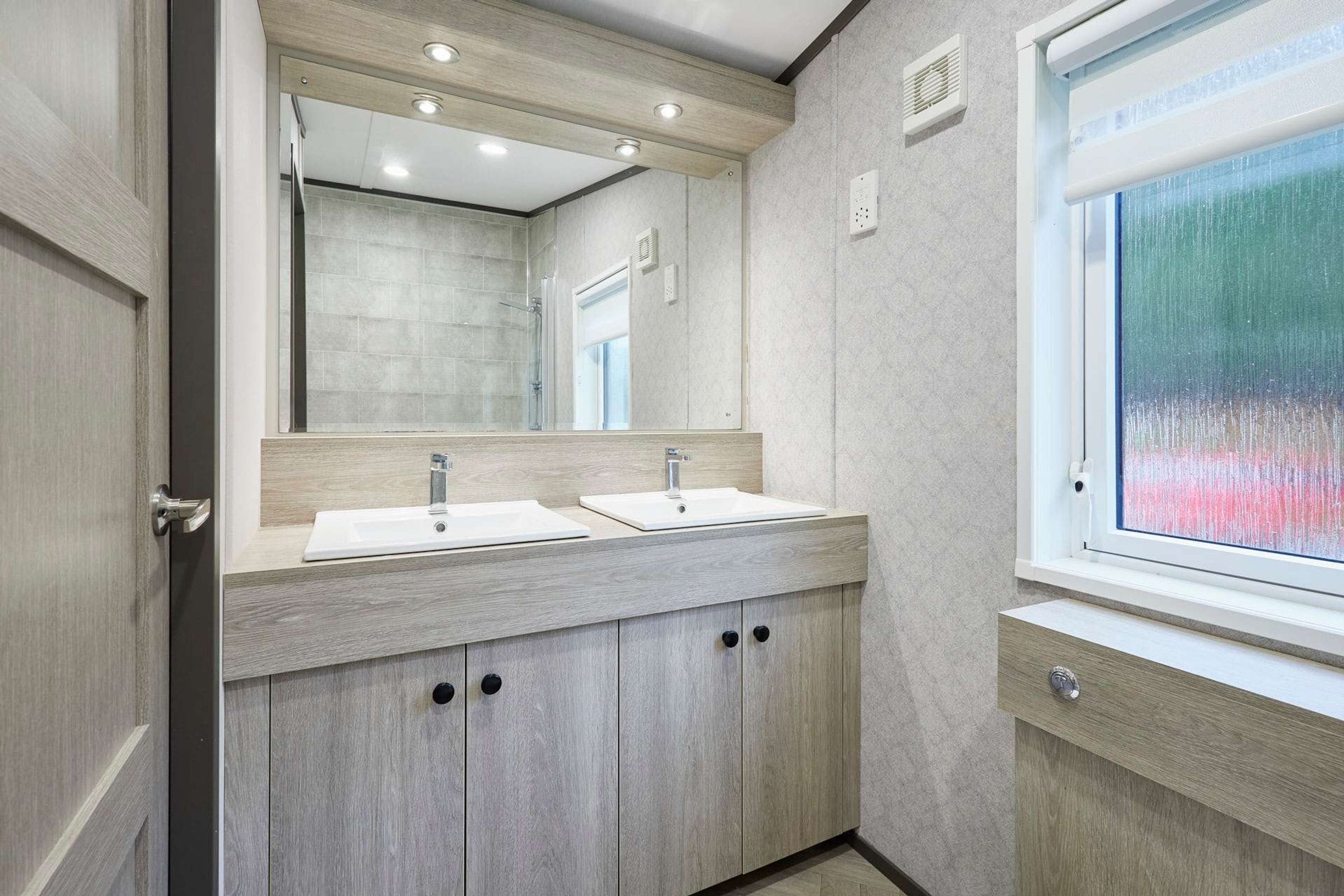 A modern bathroom with two sinks, a large mirror, and a window.