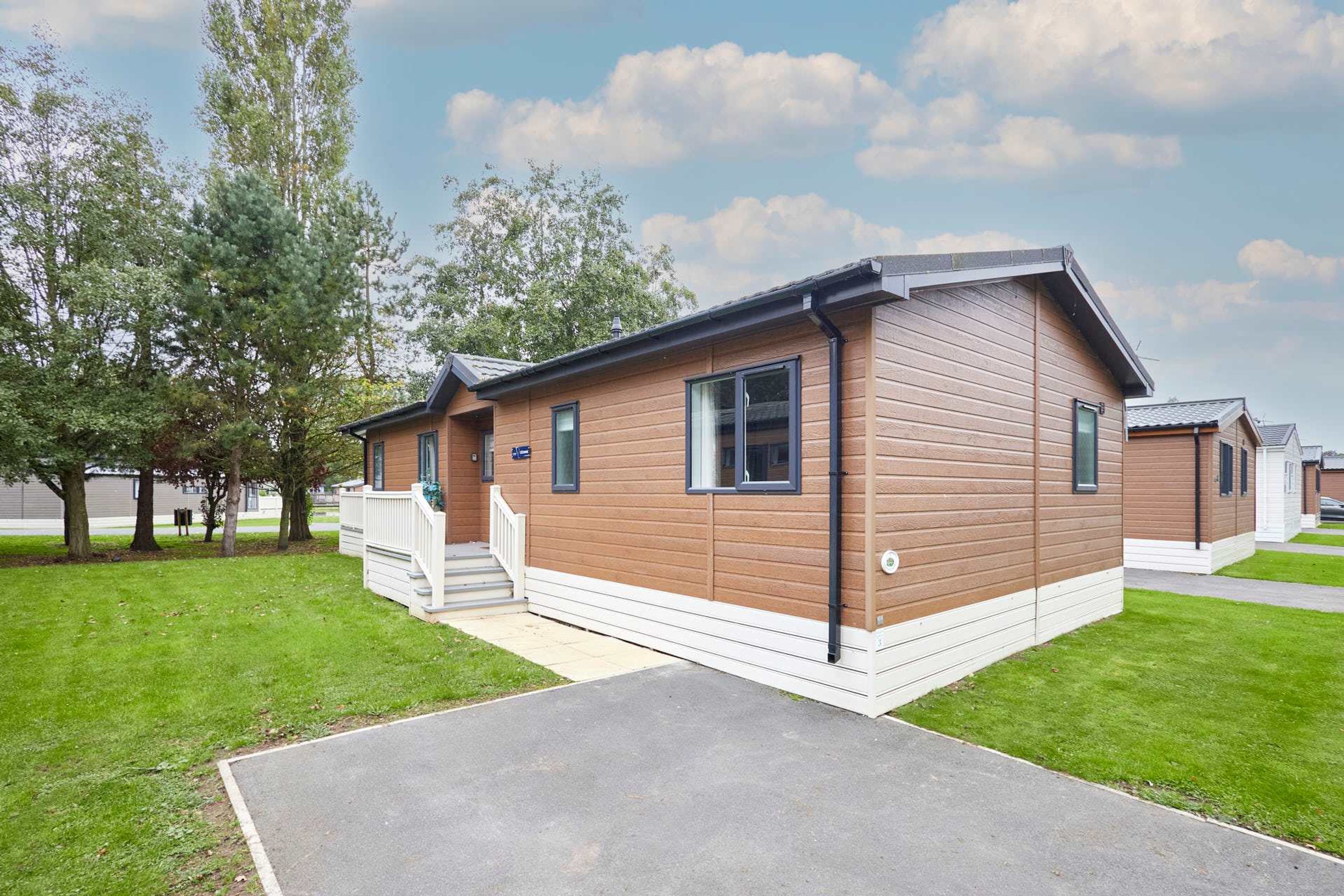 A single-story wooden cabin with a front porch, a small attached garage, and a well-maintained lawn.