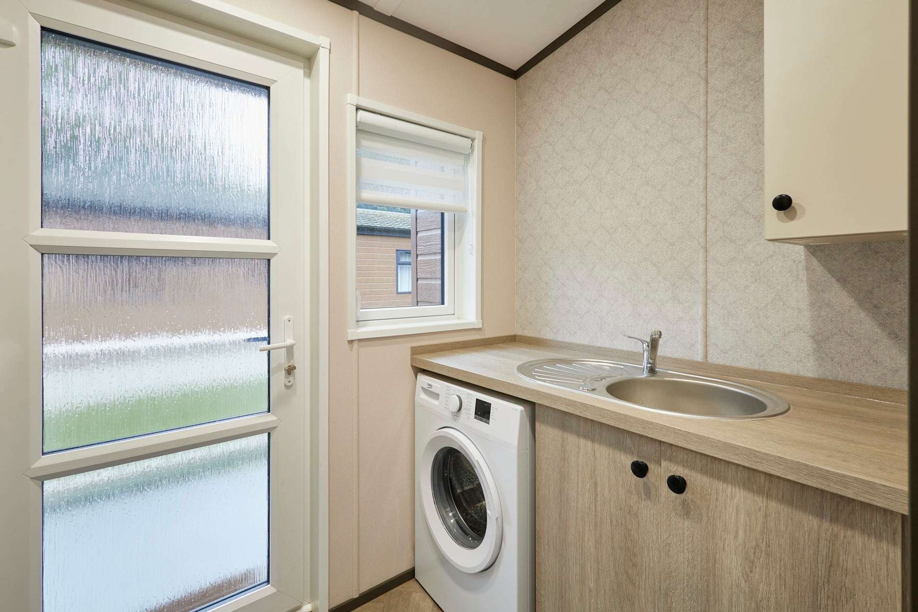 A compact laundry room with a washing machine, a sink, and a window with blinds.