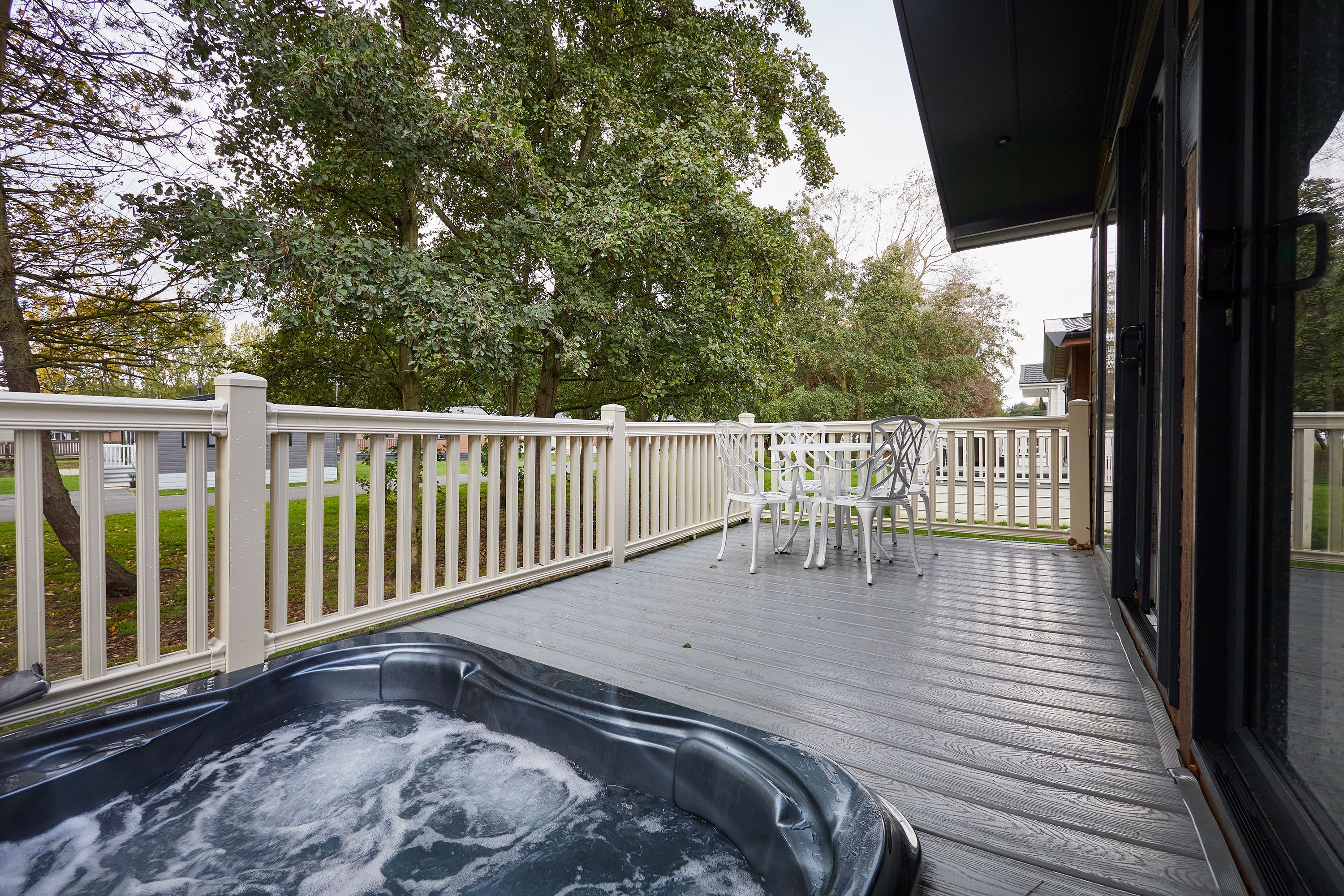 A wooden deck with a hot tub, white chairs, and a white fence.