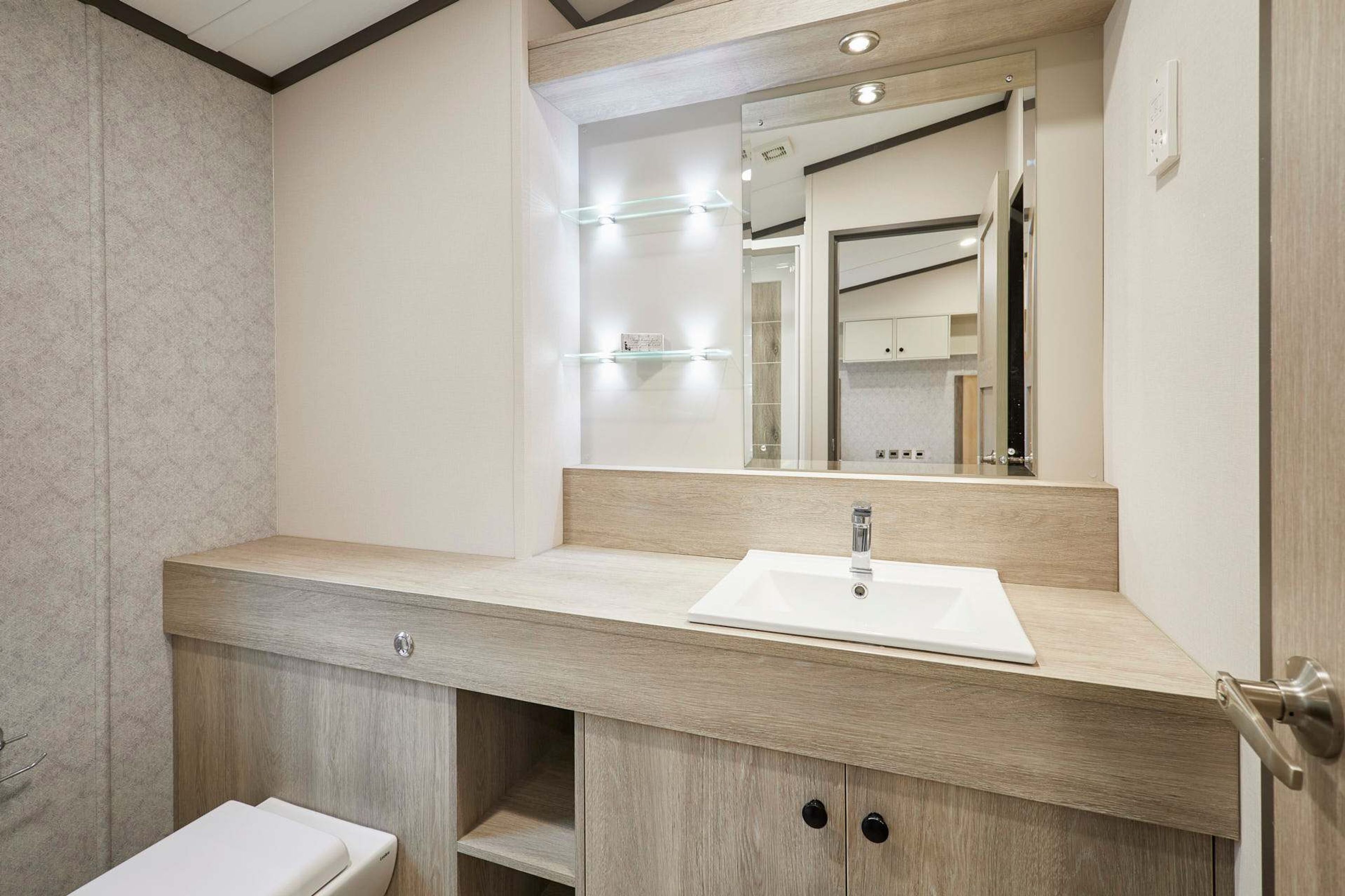 Un baño moderno con tocador de madera, un lavabo blanco y un espejo con iluminación.