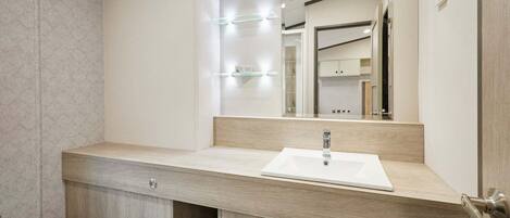 Un baño moderno con tocador de madera, un lavabo blanco y un espejo con iluminación.