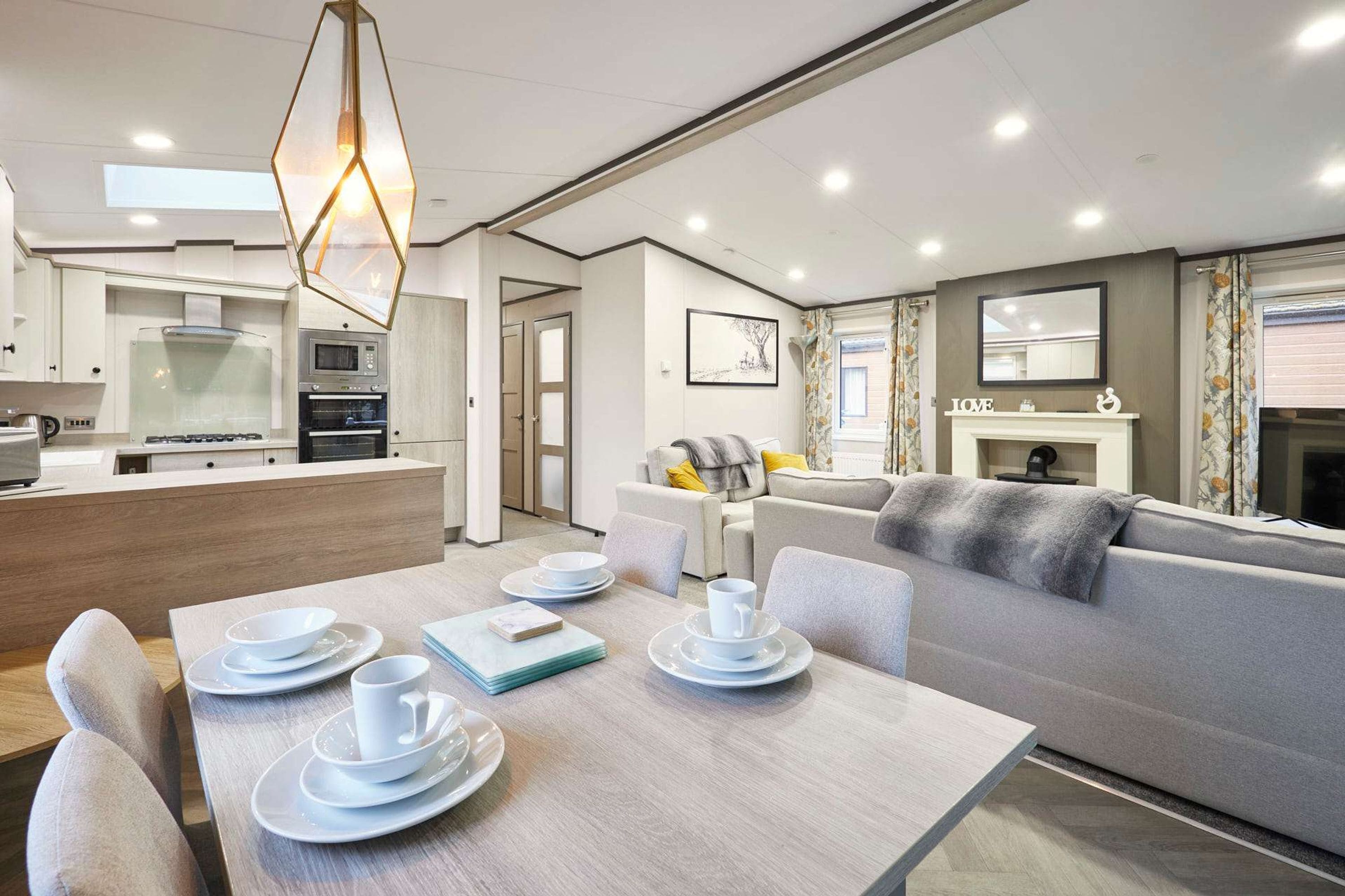 A modern kitchen with built-in appliances, a dining area with a table set for two, and a living area with a sofa and fireplace.