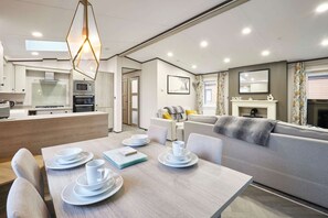 A modern kitchen with built-in appliances, a dining area with a table set for two, and a living area with a sofa and fireplace. - Host Stay Brackencroft Lodge (York)
