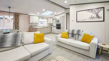 A modern living room with two white sofas, each with a yellow pillow, and a plaid throw blanket. A small round table is visible to the right.