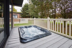 A hot tub on a wooden deck with a white fence and trees in the background.
