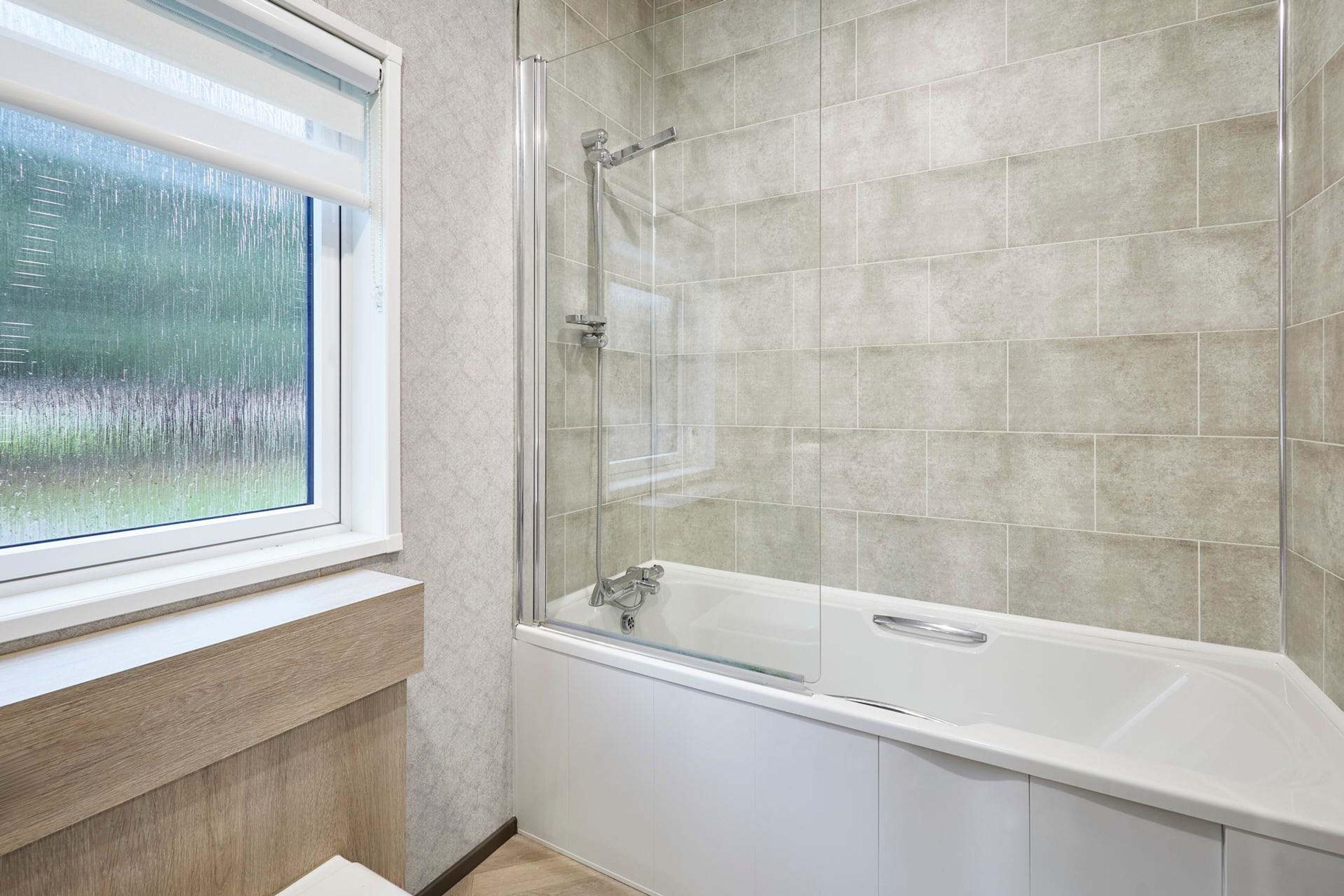 Une salle de bain moderne avec une douche à l’italienne en verre, une baignoire blanche et une fenêtre donnant sur un paysage verdoyant.