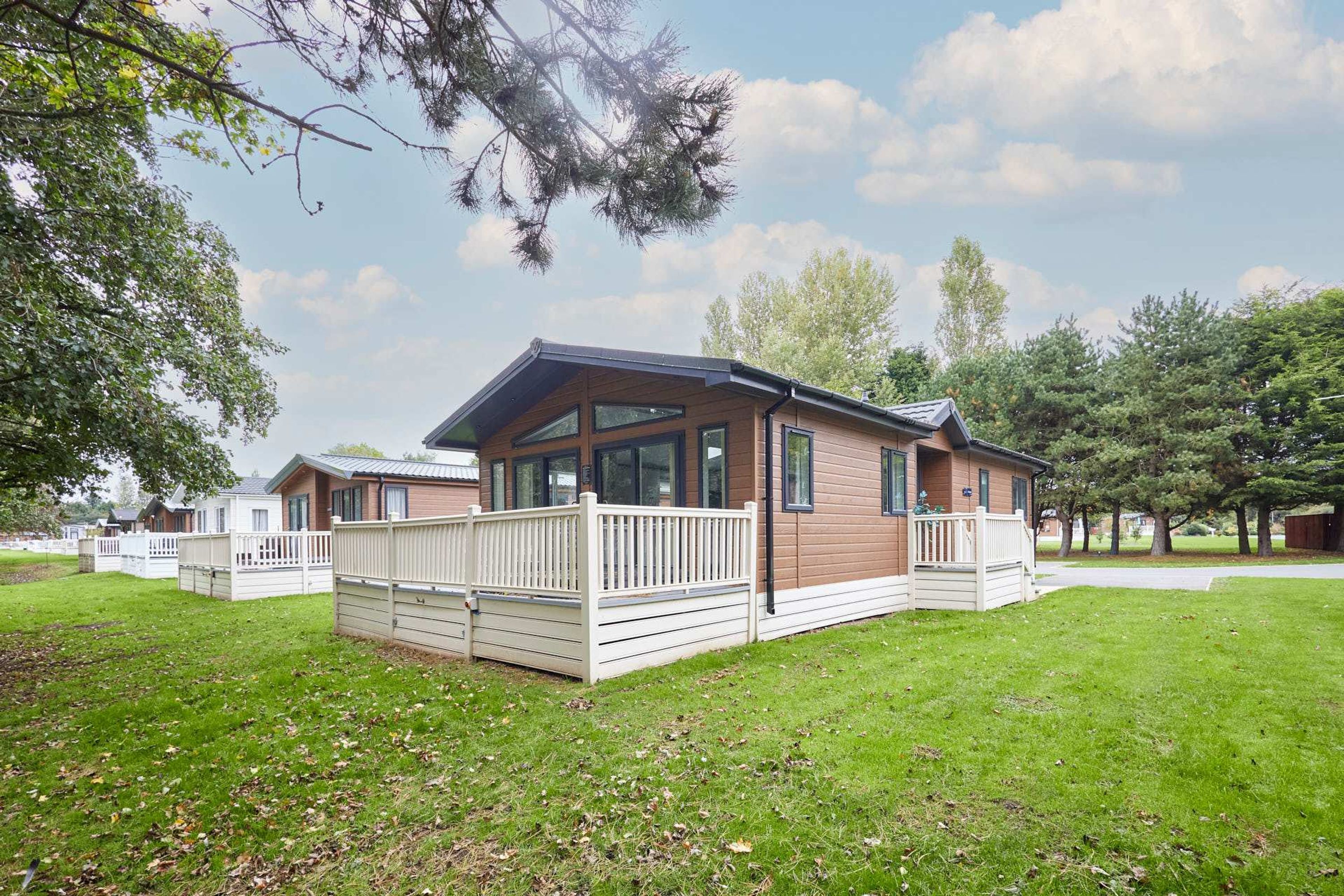 Une maison mobile moderne dotée d’une terrasse, entourée d’une pelouse et d’arbres.