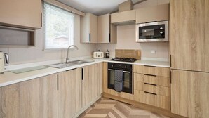 Une cuisine moderne avec des meubles en bois, un four en acier inoxydable, un four à micro-ondes et une cuisinière à gaz.