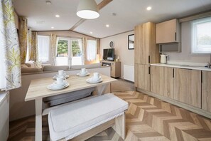 Una cocina moderna con suelo de madera en espiga, una mesa de comedor con banco y un televisor sobre un mueble.