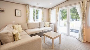 Un salon avec un canapé beige, une petite table et de grandes fenêtres avec des rideaux.