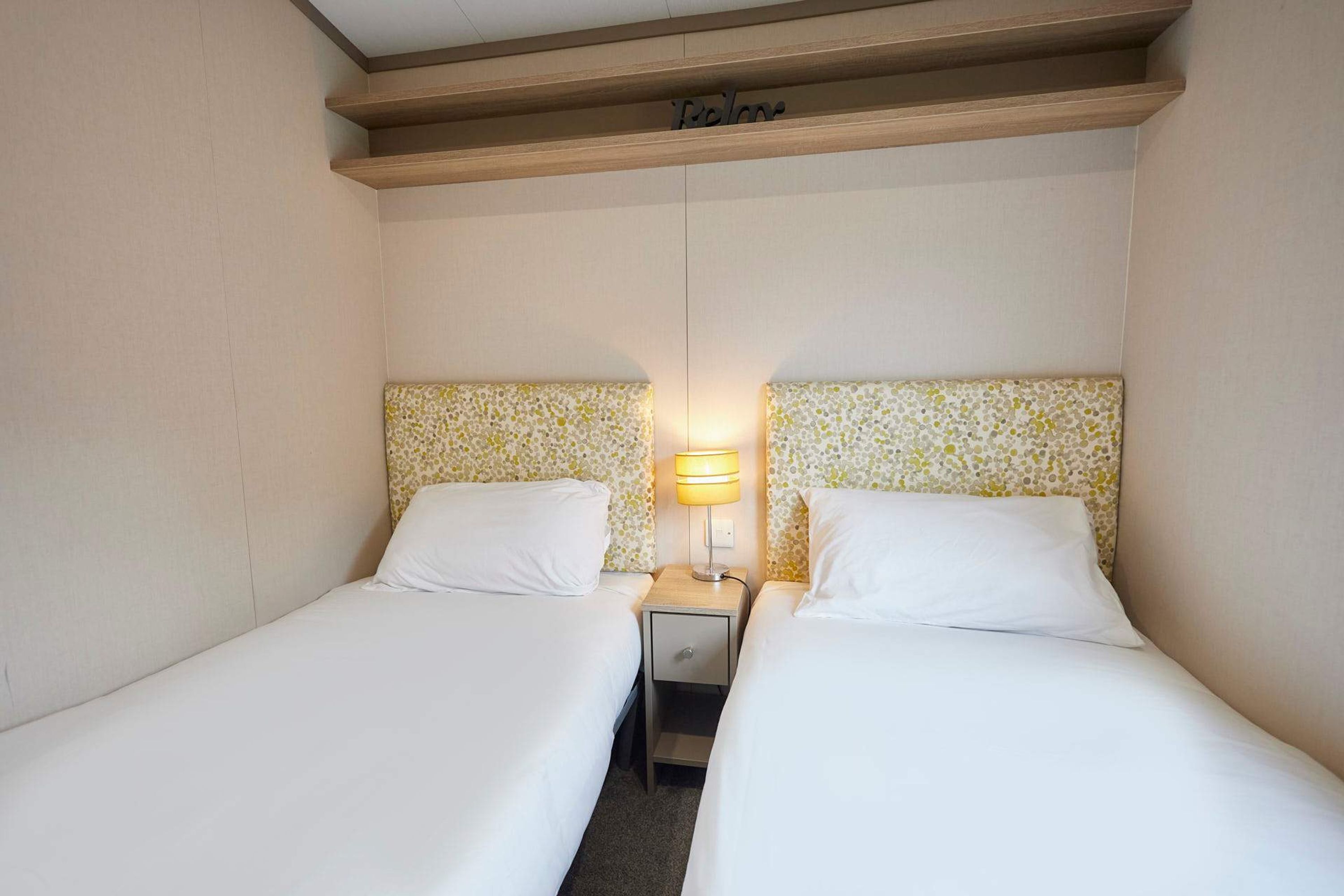 Une chambre d’hôtel avec deux lits simples, une table de chevet avec une lampe et un petit tiroir.