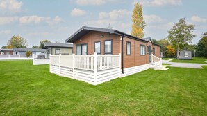 A single-story, wooden cabin with a white deck and a small porch. - Host Stay Woodpecker Lodge (York)