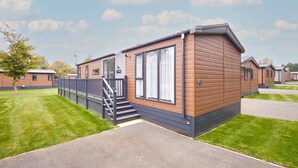 A mobile home with a wooden exterior, a staircase leading to the entrance, and a paved driveway. - Host Stay Field View Lodge (York)