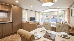 A modern kitchen with wooden cabinets, a dining area with a table set for two, and a large window providing a view of the outside. - Host Stay Field View Lodge (York)