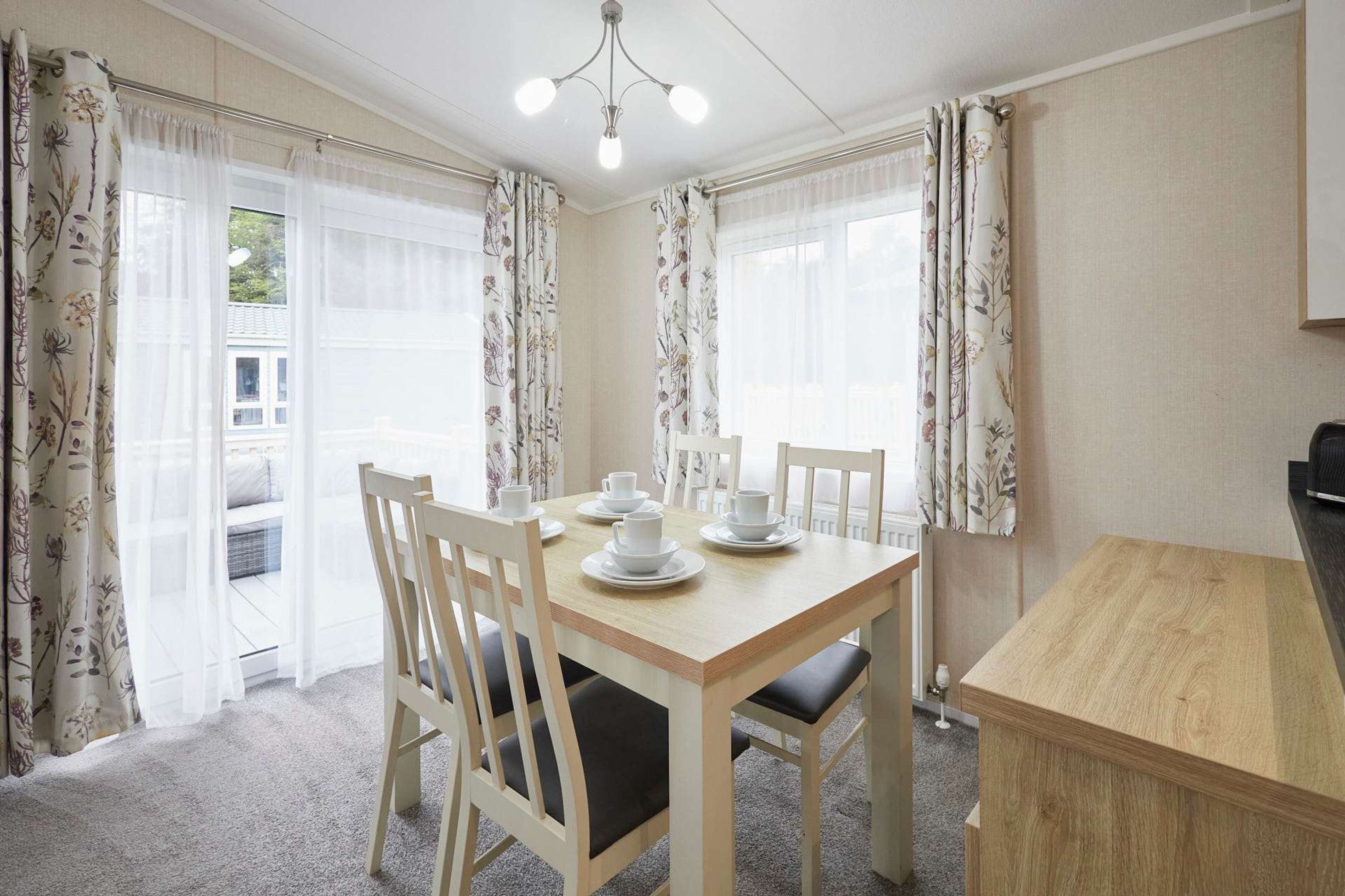 A dining area with a wooden table set for four, surrounded by white chairs with black cushions.