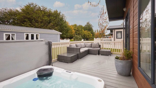A hot tub on a wooden deck with a white fence and a sofa. - Host Stay Bluebell Lodge (York)