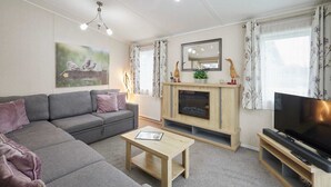 A living room with a grey sofa, a wooden coffee table, a fireplace, a television, and a painting on the wall. - Host Stay Bluebell Lodge (York)
