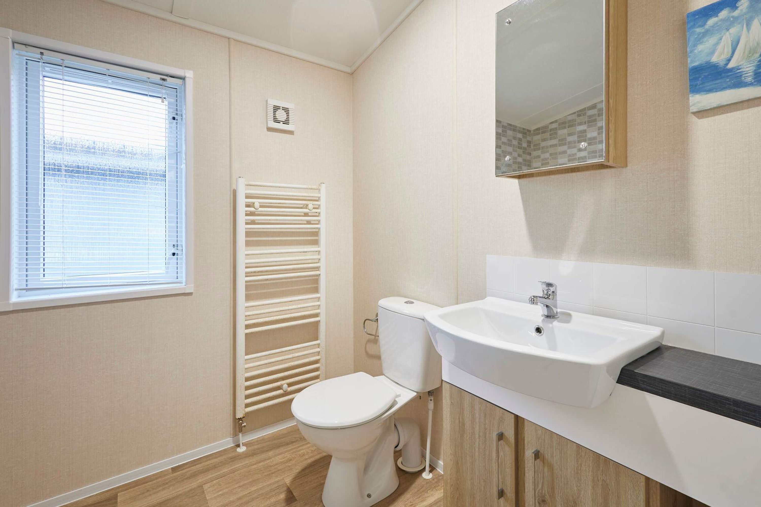 A bathroom with a toilet, a sink, a mirror, and a window with blinds.