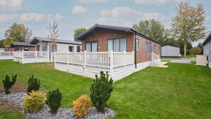 A row of mobile homes with white railings, a grassy lawn, and small shrubs. - Host Stay Bluebell Lodge (York)