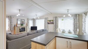 A modern living room with a sofa, a flat-screen TV, and a dining area with a table set for two. - Host Stay Bluebell Lodge (York)