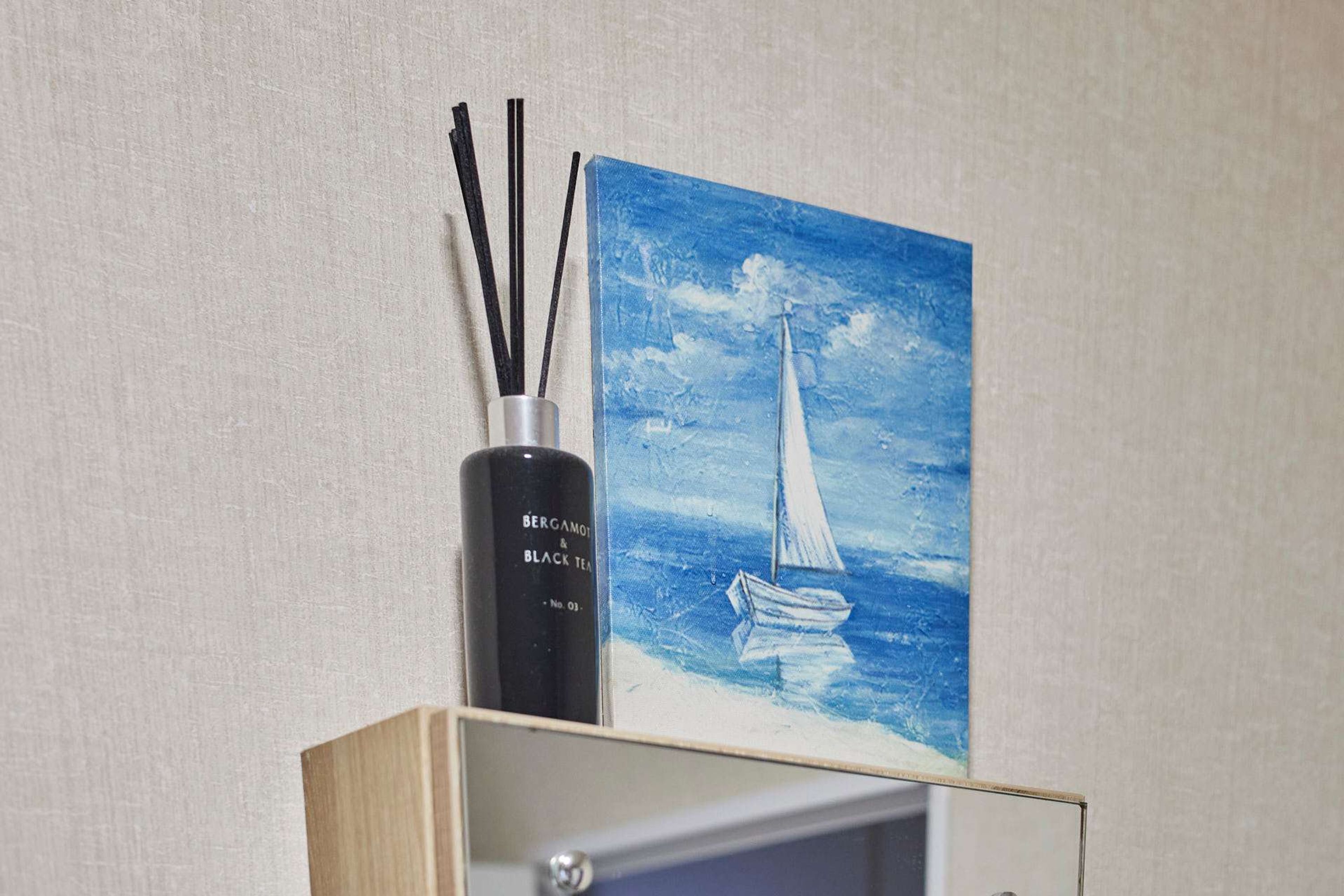 A painting of a sailboat on a blue sea, a black bottle labeled "BERGAMO & BLACK TEA," and a wooden cabinet.