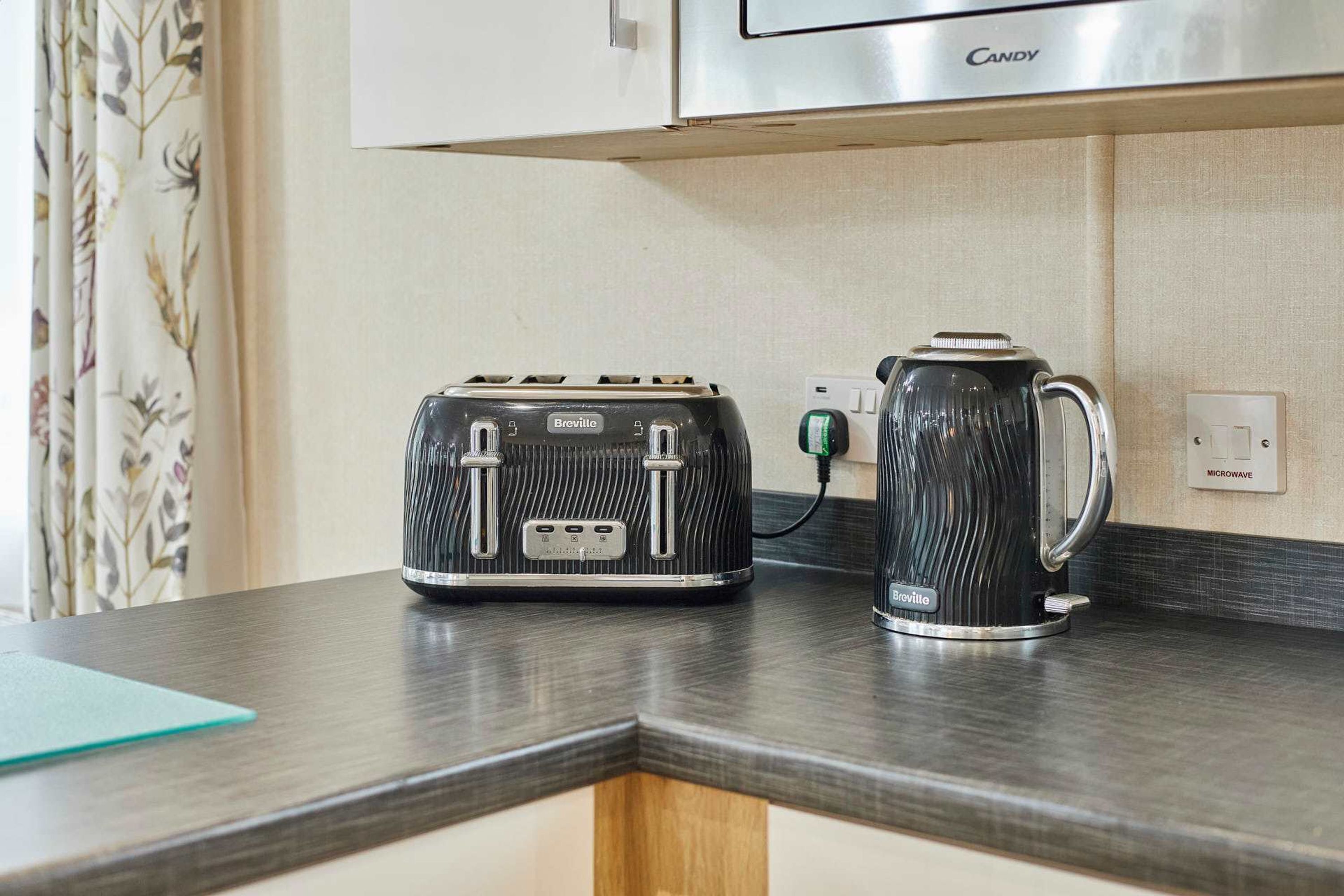 A Breville toaster and kettle on a kitchen counter with a microwave above.